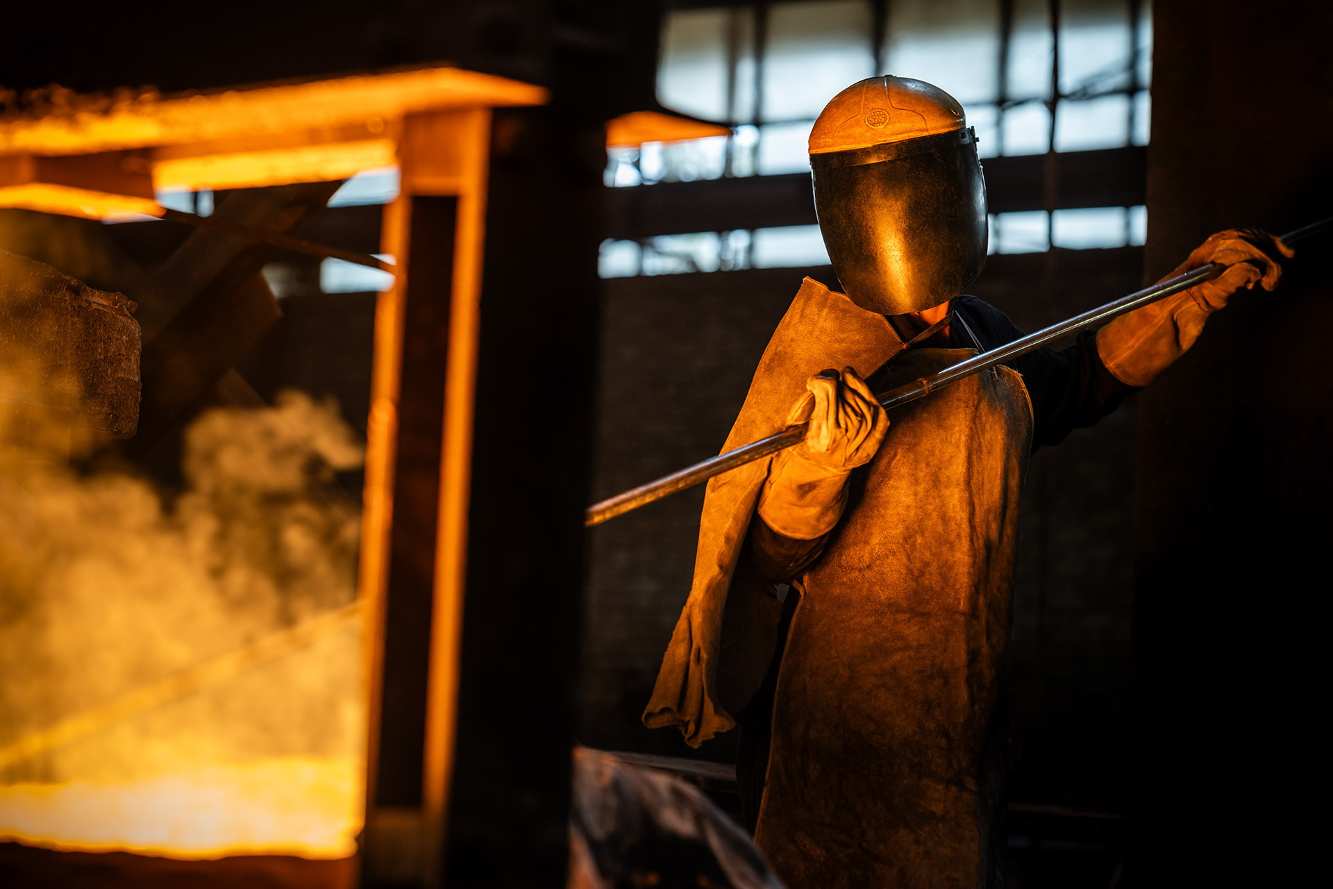 کارگر ریخته‌گری با ماسک و شیلد محافظ در نور نارنجی کوره
