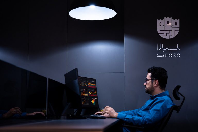 کارمند مرد در حال بررسی داده‌ها روی مانیتور در اتاق تاریک با نور متمرکز