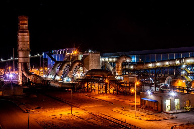 نمای شب کارخانه با لوله‌های انتقال گاز و بخارات و نورهای محیطی